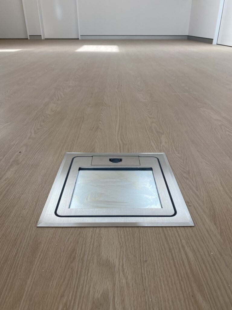 Metal floor access hatch on wooden flooring.