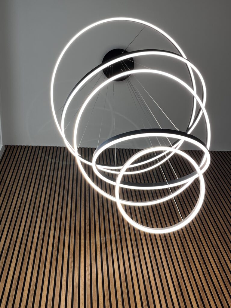 Modern circular ceiling light above wooden slatted floor.